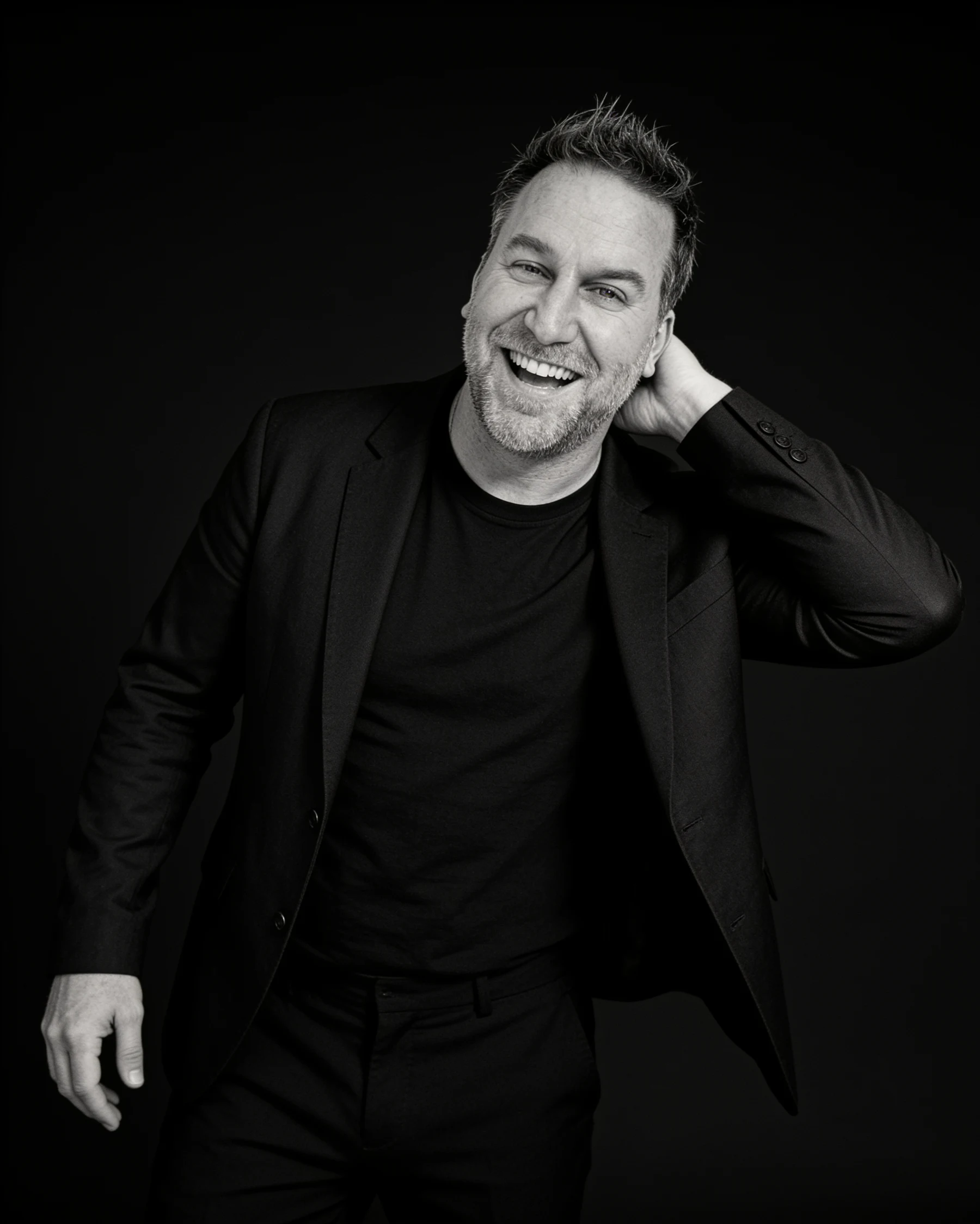 Randy Branam laughing with one hand behind his head in a monochrome studio portrait