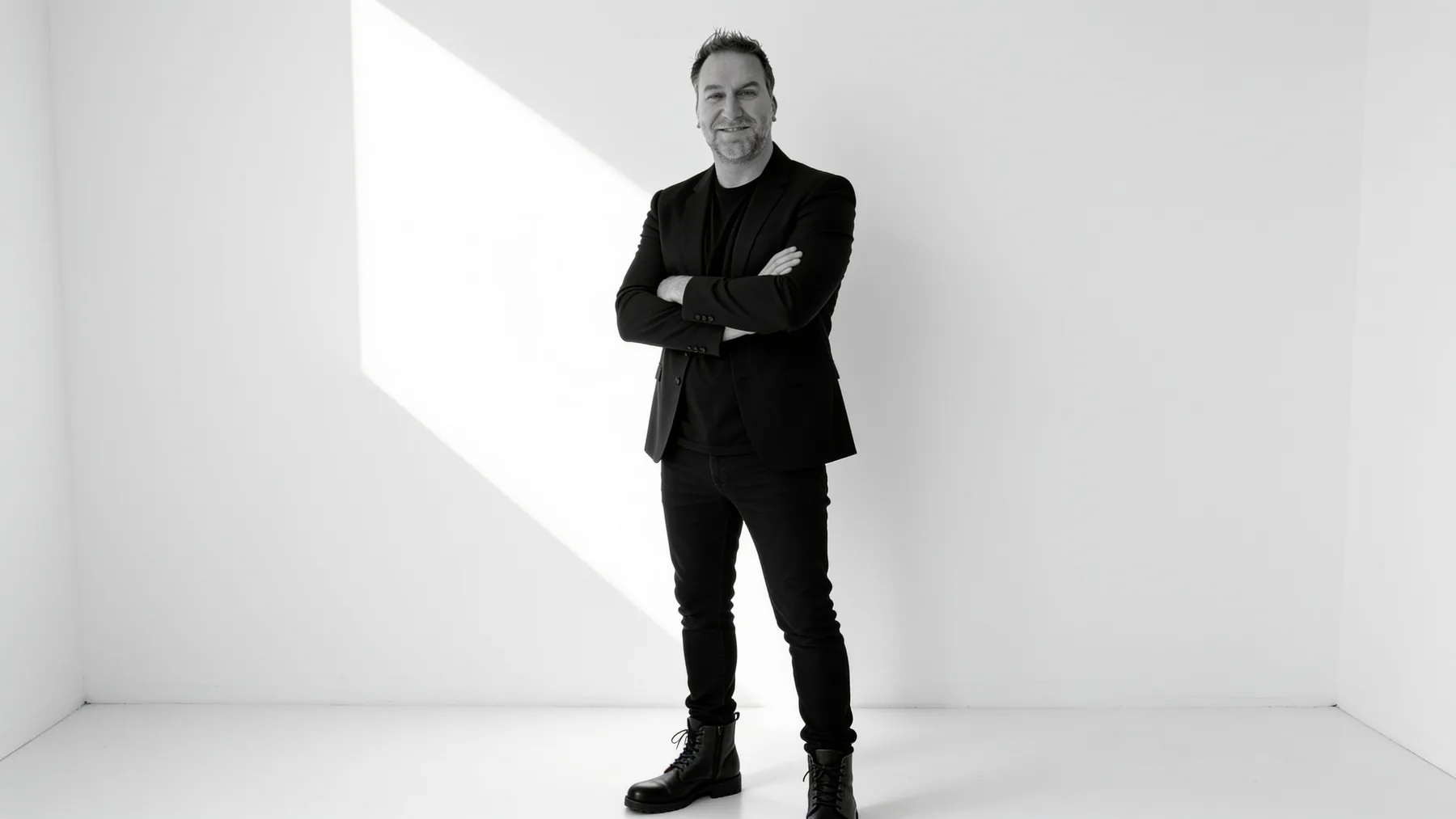 Randy Branam standing with arms crossed and smiling in a sunlit white studio