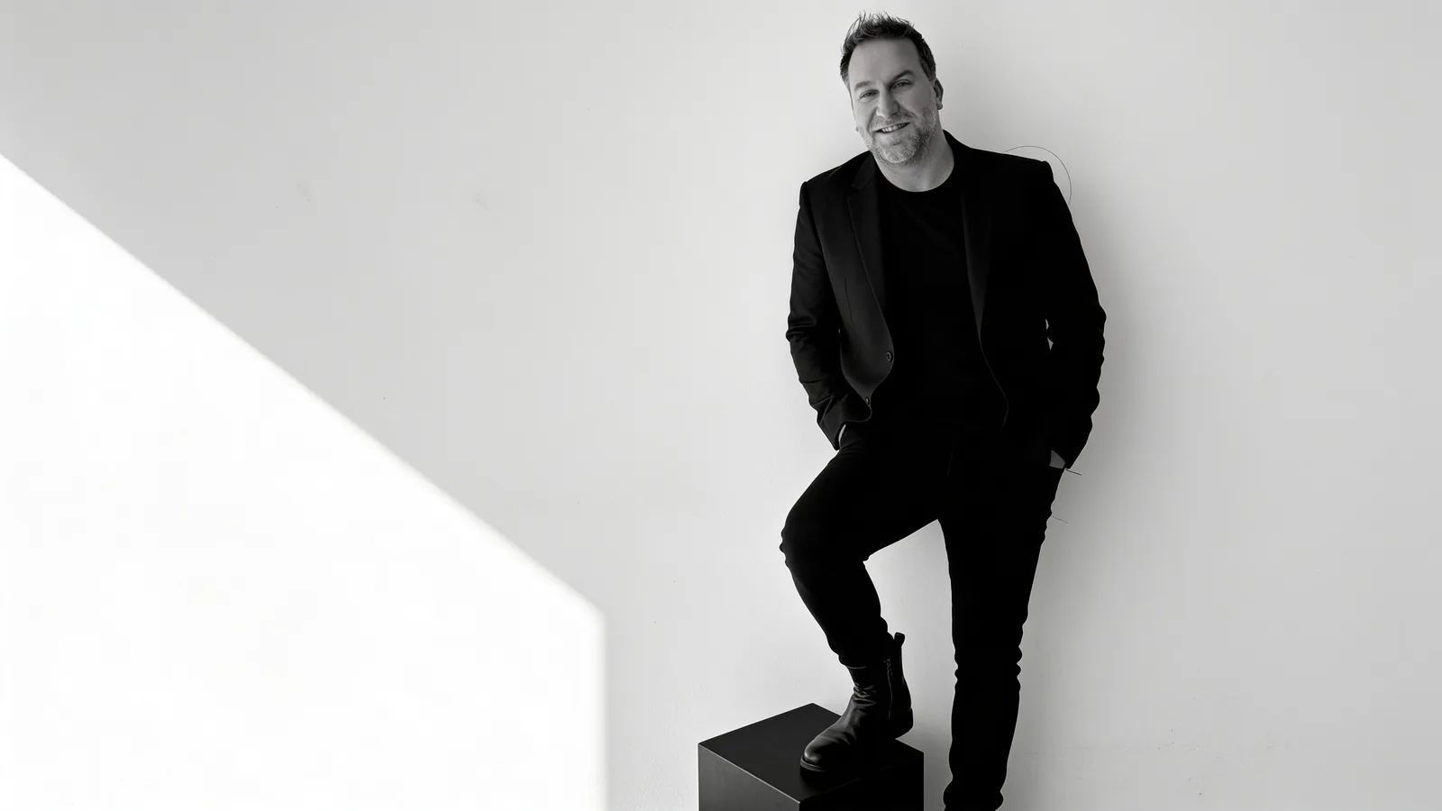 Randy Branam smiling with one foot on a black studio cube in a monochrome portrait