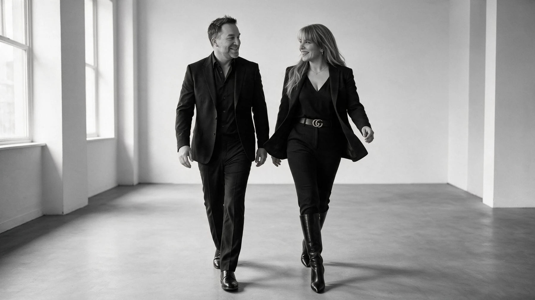 Summer and Randy Branam walking together in tailored black outfits, smiling at one another in a monochrome studio portrait