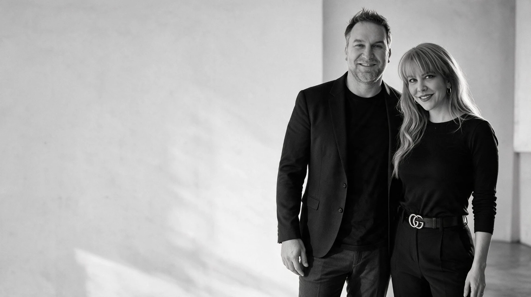 Summer and Randy Branam standing together beside studio windows in a monochrome portrait